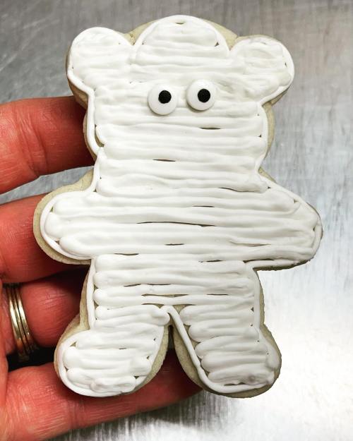 A hand holding a white frosted bear-shaped cookie with two small eyes.