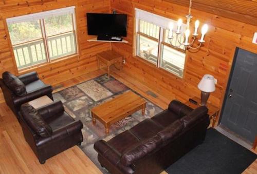 Cozy cabin living room with wooden walls, two sofas, a coffee table, TV, and a chandelier. Natural light from windows.