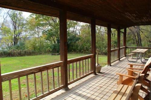 A wooden porch with chairs and a picnic table overlooks a grassy area and trees in the background.