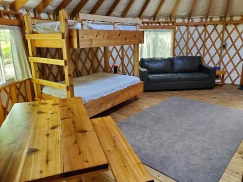 Interior of a cozy yurt featuring bunk beds, a sofa, a wooden table, and large windows for natural light.