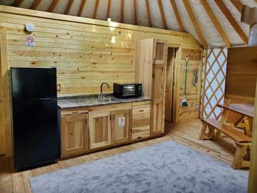 Cozy wooden kitchen interior with a fridge, microwave, sink, and a dining table in a yurt-style space.