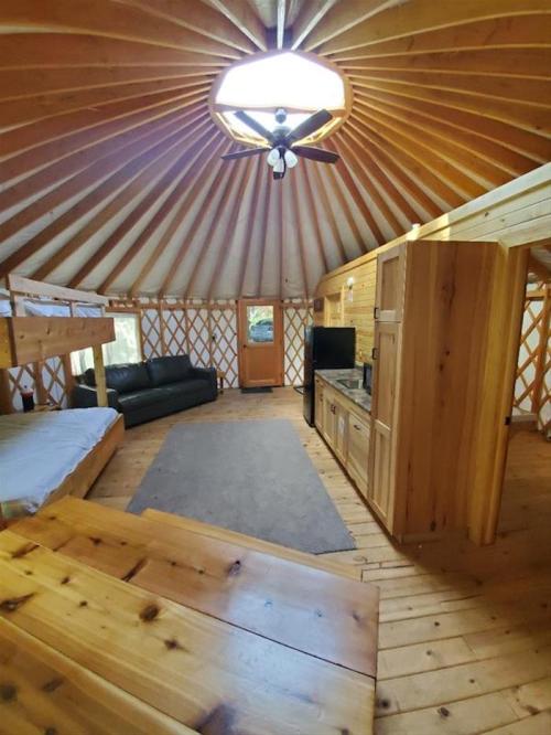 Interior of a cozy wooden yurt with a circular ceiling, bunk beds, a sofa, and a kitchenette. Natural light from the door.