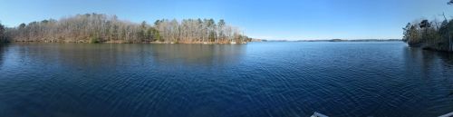Panoramic view of a calm lake surrounded by trees under a clear blue sky.