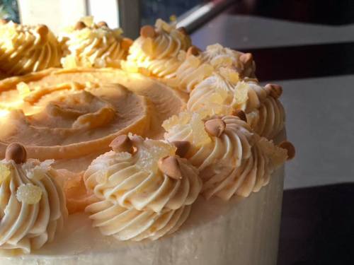 A close-up of a cake topped with swirls of creamy frosting and decorative pieces of candied ginger.