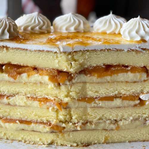 A layered cake with cream and fruit filling, topped with decorative swirls of frosting.