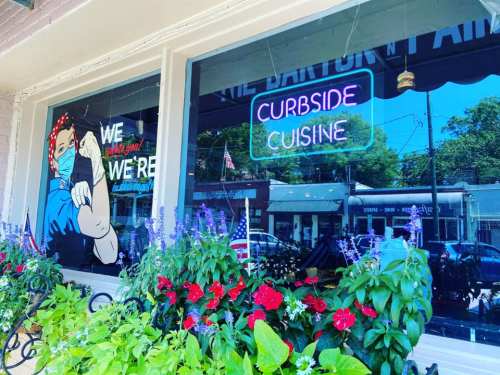 A colorful storefront with a "Curbside Cuisine" neon sign and vibrant flowers in the foreground.