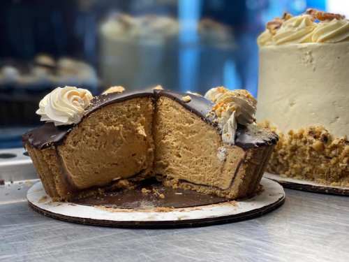 A sliced cake with a chocolate exterior and creamy filling, topped with swirls of frosting and crumbs, next to a whole cake.