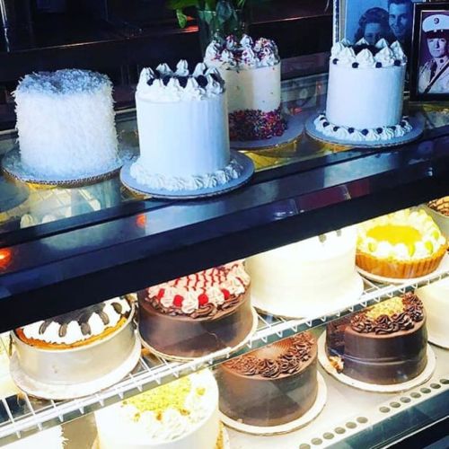 A display case filled with various decorated cakes, including white, chocolate, and colorful options.