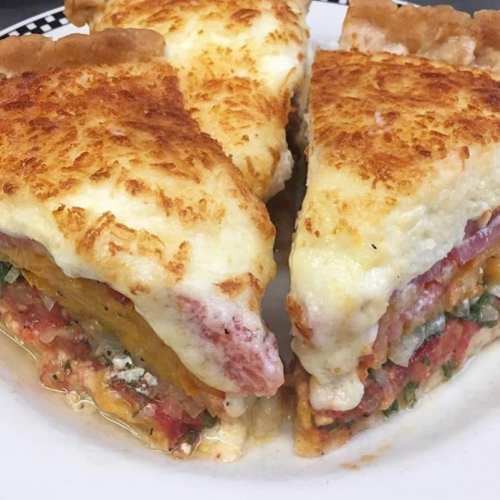 A close-up of a cheesy, layered pie with tomatoes and greens, showcasing a golden, crispy crust.