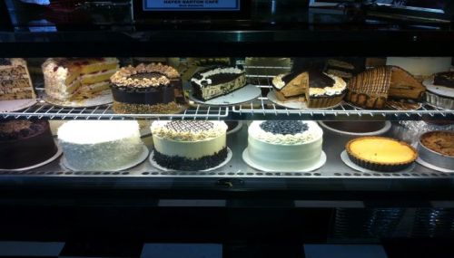 A display case filled with various cakes and desserts, including layered cakes, cheesecakes, and tarts.
