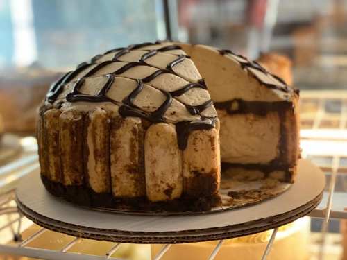 A round cake with a creamy topping, chocolate drizzle, and a slice cut out, revealing layers inside.