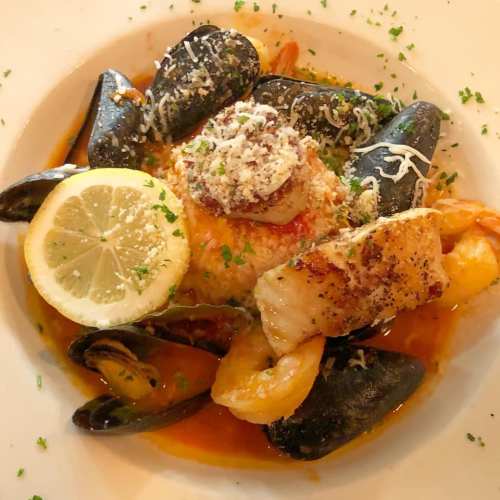 A vibrant seafood dish featuring shrimp, mussels, and fish, garnished with lemon and herbs on a white plate.
