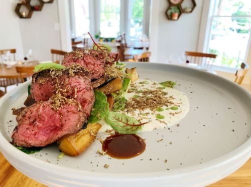 A plate of medium-rare steak with herbs, served on a bed of vegetables and a creamy sauce, garnished elegantly.