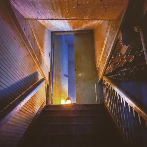 A dimly lit staircase leads to a closed door, illuminated by a lantern on the steps. The walls show signs of wear.