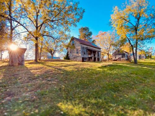 A scenic view of a historic stone house surrounded by trees and a grassy area, with sunlight peeking through.