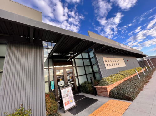 Entrance of the Hibbett Museum with a modern design, surrounded by greenery and a blue sky with clouds.