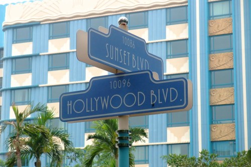 Blue street signs for Sunset Blvd and Hollywood Blvd in front of a colorful building with palm trees.