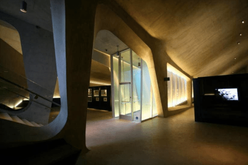 Modern interior of a museum with curved walls, soft lighting, and a glass entrance.