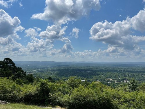 A panoramic view of lush green hills under a bright blue sky with fluffy white clouds.