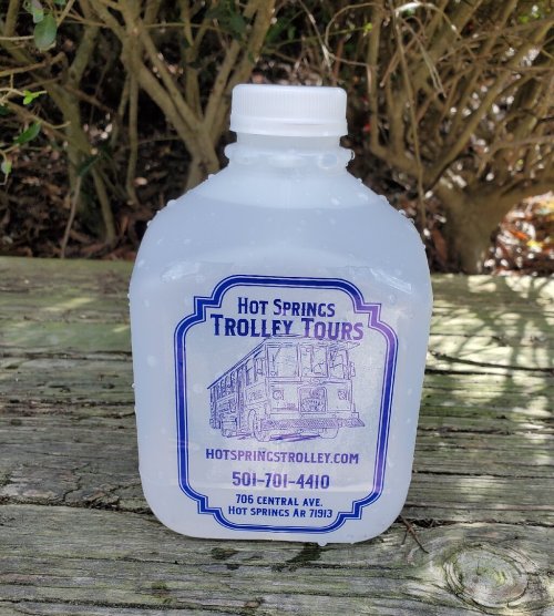 A clear water jug with a label for Hot Springs Trolley Tours, featuring contact info and website details.