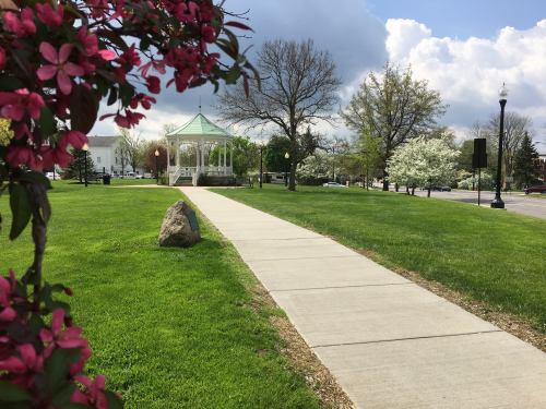 A park scene featuring a pathway leading to a gazebo, surrounded by blooming trees and colorful flowers.