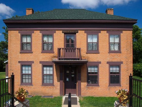 A two-story brick house with purple trim, a balcony, and large windows, set against a blue sky with clouds.