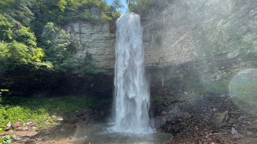 A majestic waterfall cascading down rocky cliffs, surrounded by lush greenery and sunlight filtering through the trees.