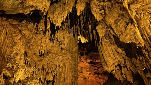 Stalactites and stalagmites in a dimly lit cave, showcasing intricate rock formations and textures.