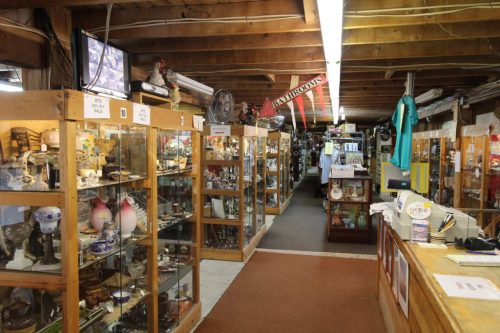 A spacious antique shop with wooden beams, glass display cases filled with collectibles, and a checkout counter.