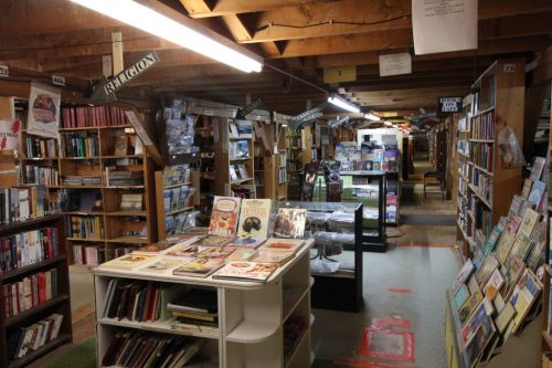 A cozy bookstore interior with wooden beams, shelves filled with books, and a display table in the center.