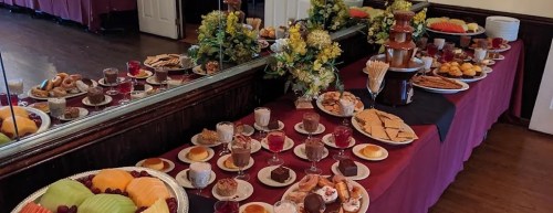A lavish dessert table featuring fruits, pastries, chocolates, and a chocolate fountain, elegantly arranged with floral decor.