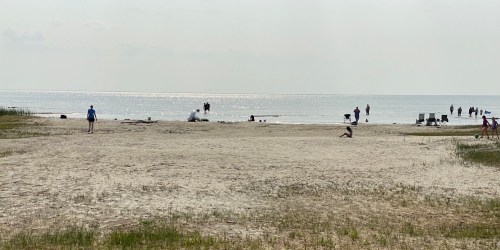 A sandy beach with people walking and relaxing near the water under a cloudy sky.