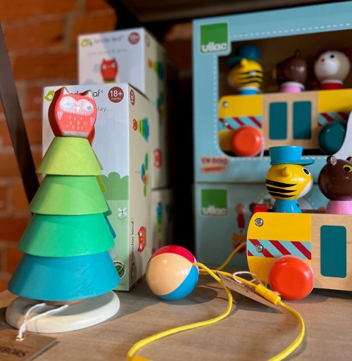 Colorful children's toys including a stacking tree, a train, and various character figures on a wooden surface.