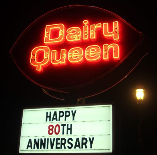 Neon sign for Dairy Queen celebrating its 80th anniversary, illuminated at night.