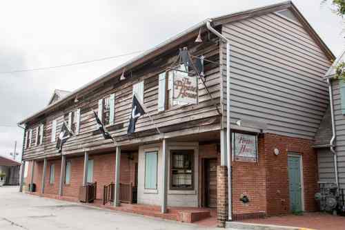 A two-story building with wooden siding and brick, featuring flags and a sign that reads "The House."