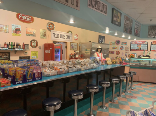 A retro candy shop with a colorful counter, vintage decor, and a staff member in a red and white uniform.