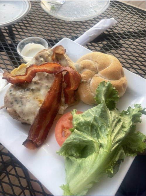 A plate with a sandwich featuring bacon, lettuce, tomato, and a side of ranch dressing on a black table.