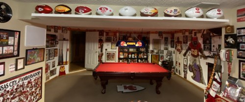 A sports-themed room featuring a pool table, framed memorabilia, and various footballs displayed on shelves.