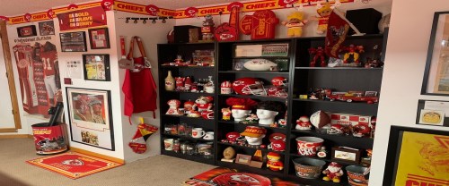 A room filled with Kansas City Chiefs memorabilia, including jerseys, helmets, and various fan items on shelves.