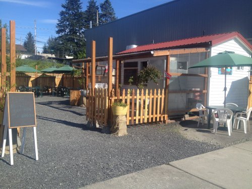 A small outdoor café with a white building, green umbrellas, and a fenced patio area on a sunny day.