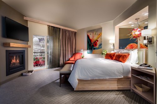 Cozy hotel room featuring a king bed, fireplace, seating area, and balcony with vibrant decor and natural light.