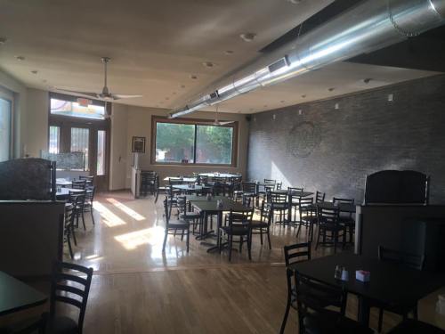 Interior of a restaurant with wooden floors, empty tables, and large windows letting in natural light.