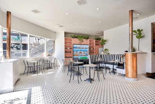 Bright café interior with black and white tiled floor, striped seating, and shelves filled with drinks.