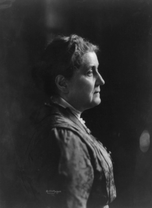 A profile portrait of a woman with curly hair, wearing a vintage dress, set against a dark background.
