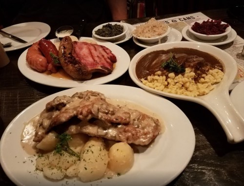 A table with various dishes: meats, sides, and sauces, including chicken, sausages, and mashed potatoes.