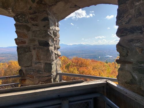 View from a stone lookout tower, showcasing vibrant autumn foliage and distant mountains under a clear blue sky.