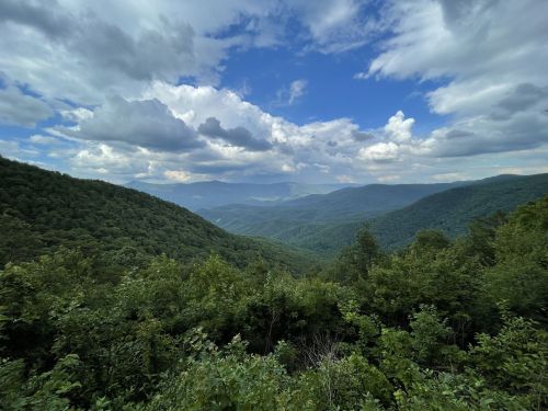 A panoramic view of lush green mountains under a partly cloudy sky, showcasing a serene natural landscape.