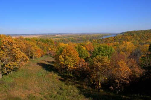 A scenic view of a river valley surrounded by vibrant autumn foliage under a clear blue sky.