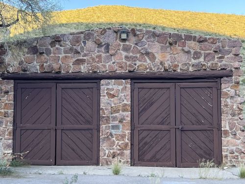 A rustic stone garage with wooden doors, set against a backdrop of golden hills.