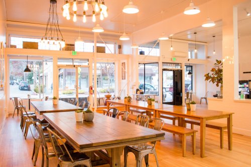 Bright, modern café interior with wooden tables, metal chairs, and large windows letting in natural light.